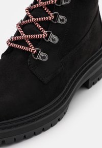Botas de senderismo de ante negro con cordones de patrón negro y rosa y ojales de metal, que presentan una suela gruesa y estriada.