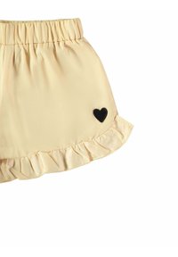 Gelbe, geraffte Shorts mit einem elastischen Bund und einem kleinen schwarzen Herzpatch an der Unterseite. Glattes Material mit einer weichen Textur.