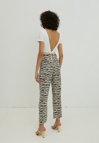 Top bianco a coste con design aperto sulla schiena, legato in vita; pantaloni pattern in beige e nero a zigzag. Sandali con tacco completano il look.