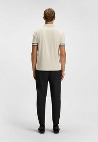 Beige Poloshirt mit schwarzen Streifenakzenten an den Ärmeln, kombiniert mit schwarzen schmalgeschnittenen Hosen. Glattes Material und ein schlichtes, minimalistisches Design.