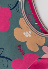 Grünes Oberteil aus Stoff mit großen rosa und beigen floralen Mustern. Gerippter Kragen in Rosa, mit weißen Akzenten und "Sigikid" in Rosa gestickt.