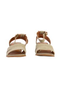 Sandales beige à bouts ouverts avec des lanières en tissu croisées et des brides autour de la cheville avec des boucles dorées, vues de face sur un fond blanc.