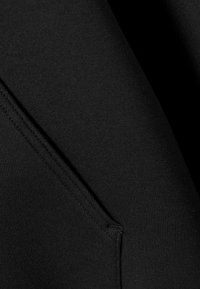 Svart sweatshirttyg nära håll, som visar en mjuk textur och en synlig söm på fickan, med rena, enkla linjer.