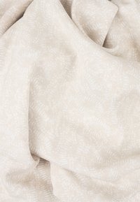 Světle béžová tkanina s jemným vzorem proplétajících se linií a teček, s měkkou, hladkou texturou, zavěšená a zmačkaná.