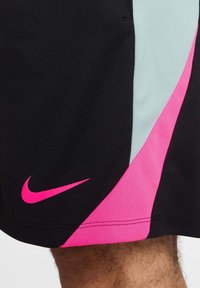Pantaloni sportivi neri con un design diagonale rosa e azzurro chiaro, con un grande logo swoosh rosa di Nike sul lato sinistro in basso.