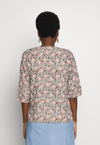 Haut à imprimé floral avec des manches trois-quarts dans des couleurs douces ; présente des motifs corail, noir et vert sur un fond clair.