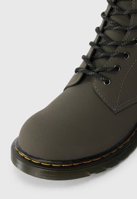 Botoșei impermeabili de culoare verde închis, cu vârf rotunjit, șireturi negre și cusături galbene pe talpă. Material neted cu accente texturate.