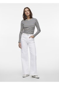 Top de manga larga de rayas y canalé en azul marino y crema, combinado con pantalones anchos blancos. Tela texturizada y diseño de cinco bolsillos visible.