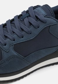 Navy blue sneaker featuring a mix of suede and mesh materials, round toe, textured accents, and flat black rubber sole with white trim.