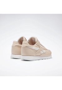 Paire de baskets Reebok beige avec des détails blancs et des semelles blanches, vues sous un angle arrière trois quarts sur un fond blanc uni.