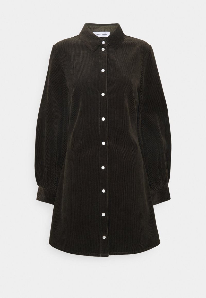 Robe en velours côtelé brun foncé à manches longues avec col et boutons blancs sur le devant, avec des manches légèrement bouffantes munies de poignets.
