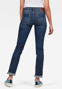 Mörkblå denimjeans med smal passform, utrustade med en läderlapp vid midjan och uppvikta fållar. Femfickorsdesign med subtila sömmar.