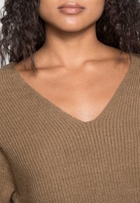 Bruine gebreide trui met een V-hals en een geribbelde structuur. Lichtgewicht stof met een zachte, gladde afwerking.