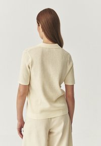 Maglietta a maniche corte lavorata a maglia in beige chiaro con un motivo testurizzato e un colletto morbido. Presenta una vestibilità rilassata e orlo a coste.