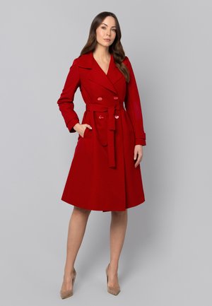 Czerwona trencz z nadrukiem w kropki, dopasowana w talii, z podwójnymi guzikami, klapami i pasującym paskiem. Gładki materiał z rozkloszowanym dołem.