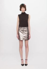 Rjav brezrokavnik s turtleneck izrezom v kombinaciji z metalno srebrno mini krilom, ki ima sprednje gumbno zapiranje in eleganten silhuet.