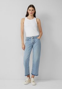 Helles blaugraues Denim-Jeans mit einer lässigen Passform und fransigem Saum, kombiniert mit einem weißen gerippten Tanktop und cremefarbenen Sneakers.