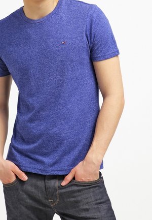 Niebieska, melanżowa bawełniana koszulka z okrągłym dekoltem i krótkimi rękawami, z małym logo marki na piersi, zestawiona z ciemnymi dżinsami.