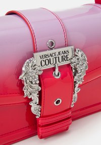 Różowa i czerwona torebka z lakierowanej skóry z srebrnymi akcentami, z ozdobnym zapięciem i etykietą "VERSACE JEANS COUTURE".