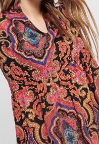Robe à motifs mettant en avant une palette de couleurs vibrantes de rose, violet et orange sur un fond noir, avec des motifs de paisley et de fleurs.