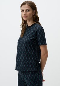 Top a maniche corte in navy con un motivo geometrico in teal. Realizzato in tessuto morbido con una vestibilità rilassata e scollo rotondo.