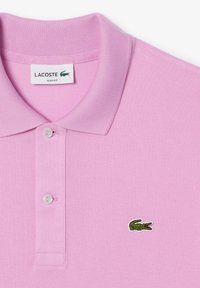 Ljusrosa polo med strukturerad tyg, med en treknappsknäppning och en grön krokodillogo på bröstet. Slim fit-design.