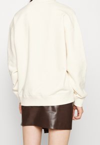 Överdimensionerad krämfärgad sweatshirt med rund halsringning och sänkta axlar, tillsammans med en glänsande brun faux läderkjol.