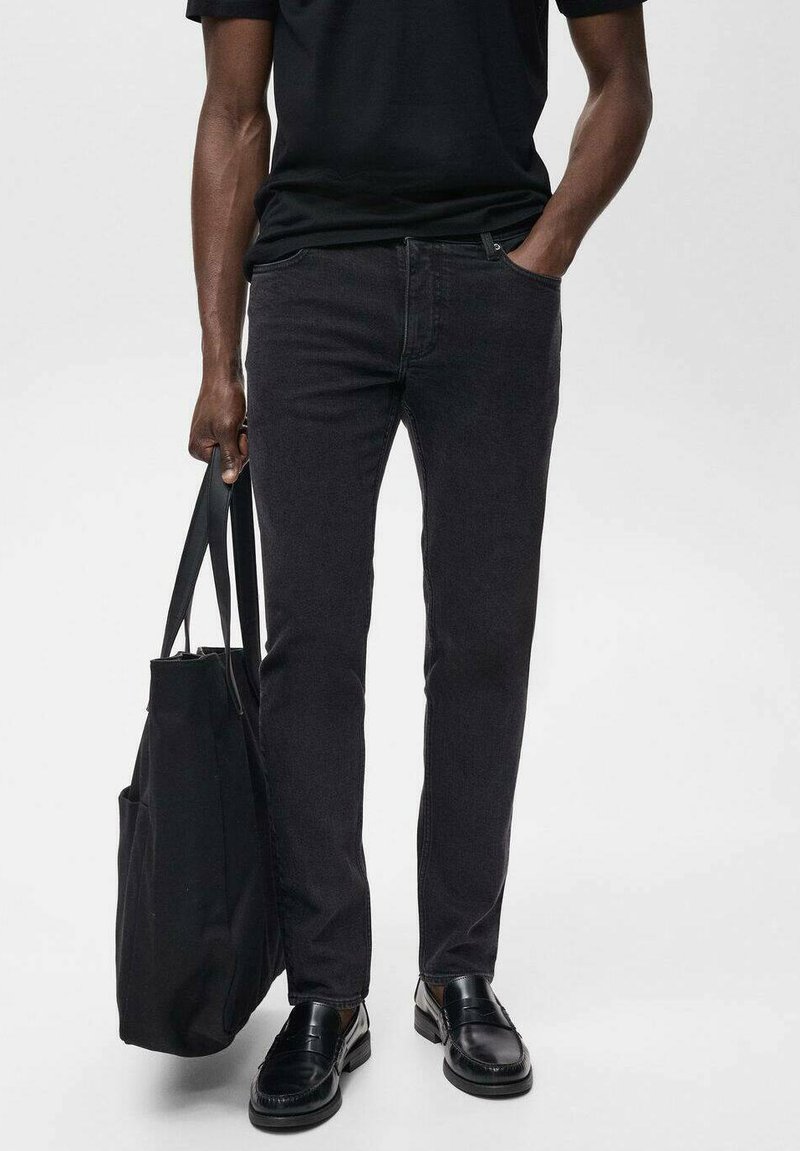Jeans de mezclilla negra con un ajuste slim, combinados con una camiseta negra y zapatos de cuero negros, sosteniendo una bolsa tote negra. Textura suave, diseño sencillo.