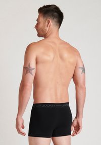 Svarta herrboxershorts med en logotyp på midjebandet, tight passform, mjuk textur och låg skärning, visade bakifrån på en modell.