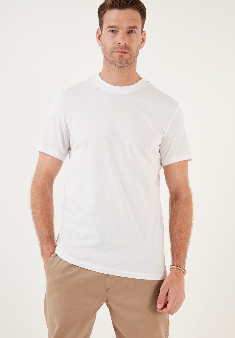 T-shirt bianco in cotone con scollo rotondo e maniche corte, caratterizzato da una texture liscia e una vestibilità comoda. Abbinato a pantaloni beige.