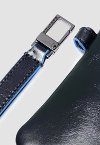 Cinturino in pelle blu navy con cuciture blu e componenti in metallo, caratterizzato da una chiusura rettangolare. Texture liscia e finitura lucida sulla pelle.