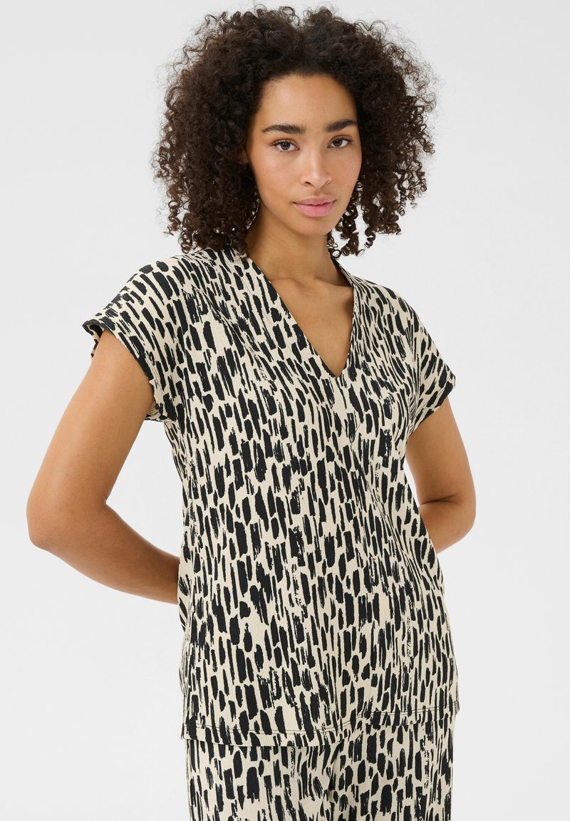 Haut à manches courtes noir et ivoire avec un décolleté en V, présentant un motif abstrait audacieux et une coupe décontractée, fabriqué à partir d'un tissu léger.