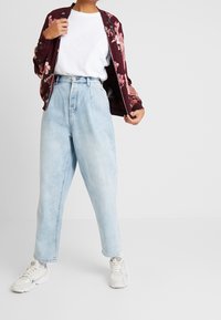 Burgundowa bomberka z kwiatowym wzorem, biała koszulka, jasnoniebieskie jeansy z wysokim stanem i białe trampki. Miękka tkanina i luźny krój.