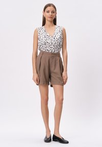 Biała bluzka bez rękawów w kwiatowy wzór zestawiona z brązowymi szortami o wysokim stanie, z kontrafałdami i podwiniętymi brzegami. Czarne buty typu slip-on.