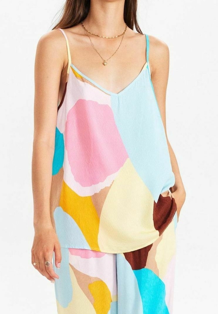 Femme portant un haut ample sans manches et un pantalon avec des formes abstraites colorées dans des tons pastel rose, bleu, jaune et marron.
