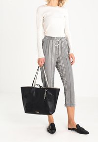 Mustat tekstuurella varustettu olkalaukku, jossa on kukkakoristeita, vaaleanruskea sisus ja kaksinkertaiset olkahihnat. Yhdistetty raitapaitoihin ja valkoiseen pitkähihaiseen toppiin.