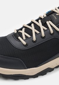 Chaussure de randonnée en maille noire avec des lacets beiges, une semelle intermédiaire beige et une semelle extérieure noire robuste, avec le logo Columbia près du premier œillet.