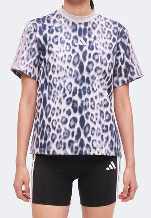 Osoba nosząca koszulę z krótkim rękawem w panterkę z logo adidas oraz czarne spodenki z białymi paskami i logo adidas.