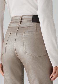 Pantalons taille haute beige métallique avec poches arrière et un accent en cuir noir à la taille. Texture lisse avec un léger éclat.