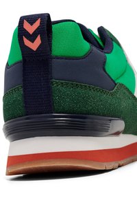 Grønn og marineblå joggesko med en teksturert stoffoverdel, napa-detaljer, en pull tab med oransje aksenter, og en gummisåle med en rød stripe.