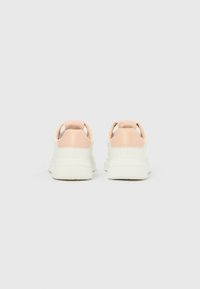 Hvite plattform-sneakers med lyserosa hældetaljer vist bakfra mot en enkel, lys grå bakgrunn.