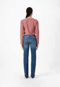 Röd- och vitrutig långärmad topp kombinerad med tajta blå jeans. Jeansen har bakfickor och en brun läderdetalj.