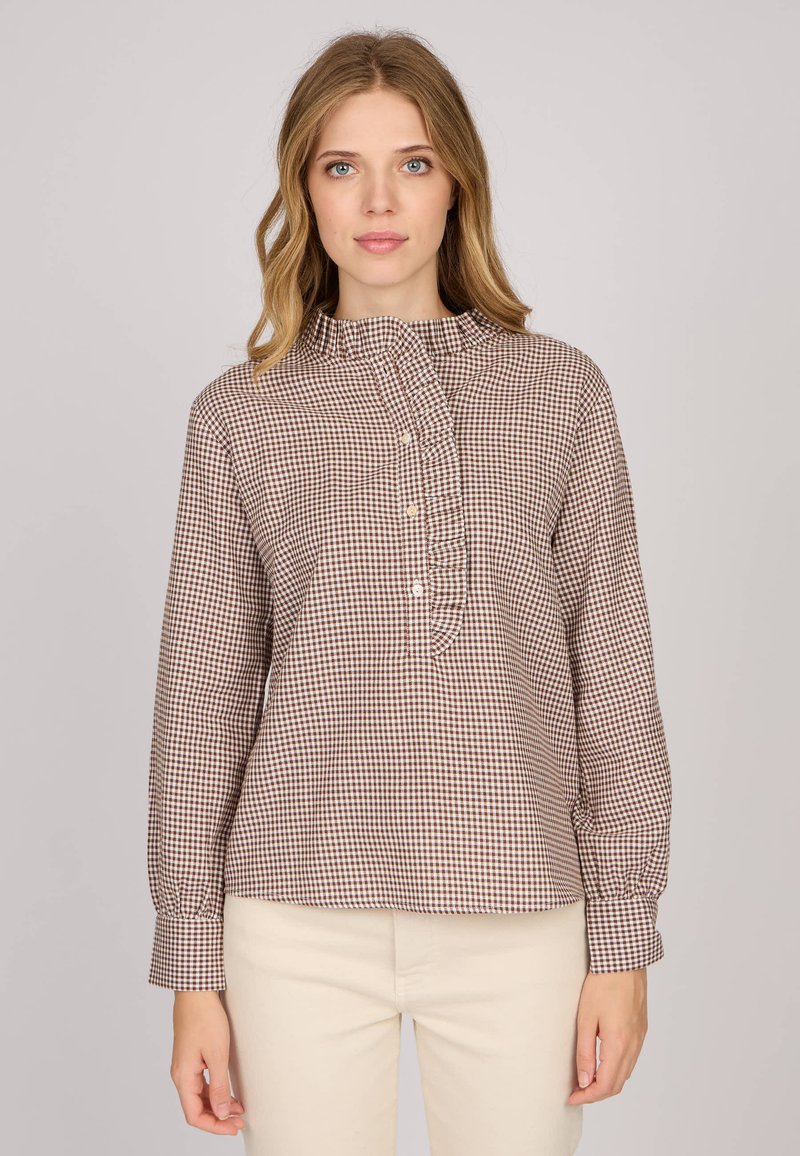 Chemise à carreaux marron et blanc avec un col volanté et des manches longues. Le tissu a une texture lisse, des poignets ajustés et une coupe décontractée.