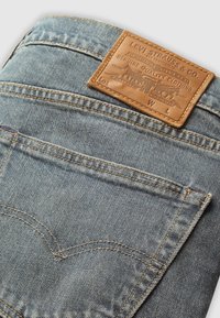 Gros plan sur la poche arrière d'un jean en denim bleu clair avec des coutures visibles et une étiquette en cuir marron de la marque Levi Strauss attachée au-dessus de la poche.