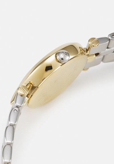 Vue latérale d'un boîtier de montre en or et argent avec une couronne et deux boutons-poussoirs sur un bracelet en métal argenté à maillons.