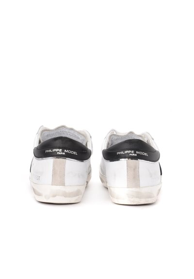 Sneakers bianchi in pelle con dettagli neri, una superficie liscia, suole in gomma piatta e un logo sul tallone. Aspetto usurato sulle suole.