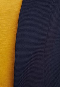 Yellow and navy fabric pieces, one smooth and one textured, overlap at the edge, displaying distinct colors and materials.