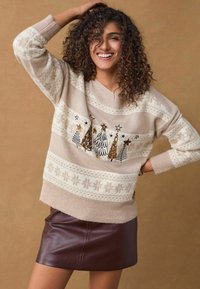 Maglione beige lavorato a maglia con motivo di fiocchi di neve bianchi e un design di albero di Natale con dettagli dorati luccicanti. Abbinato a una mini gonna in similpelle bordeaux.
