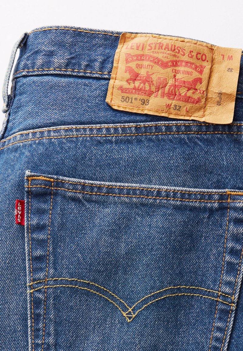 Vaqueros de mezclilla azul con una etiqueta de cuero que muestra "Levi Strauss & Co." y detalles del estilo. Presenta costuras amarillas y una etiqueta roja en el bolsillo.