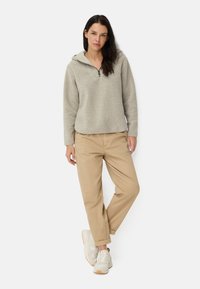 Lichtgrijze fleece pullover met een halve rits kraag, gecombineerd met beige ruime broek en witte sneakers met bruinaccenten.